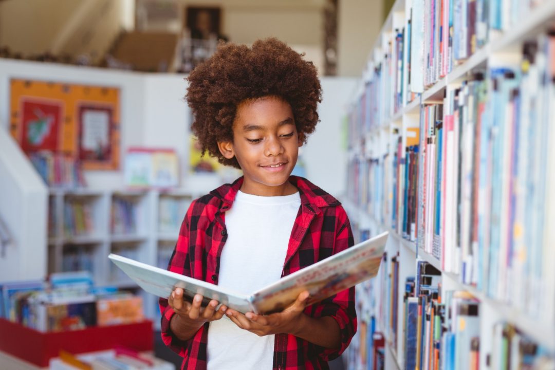 smiling-african-american-schoolboy-reading-book-standing-in-school-library.jpg